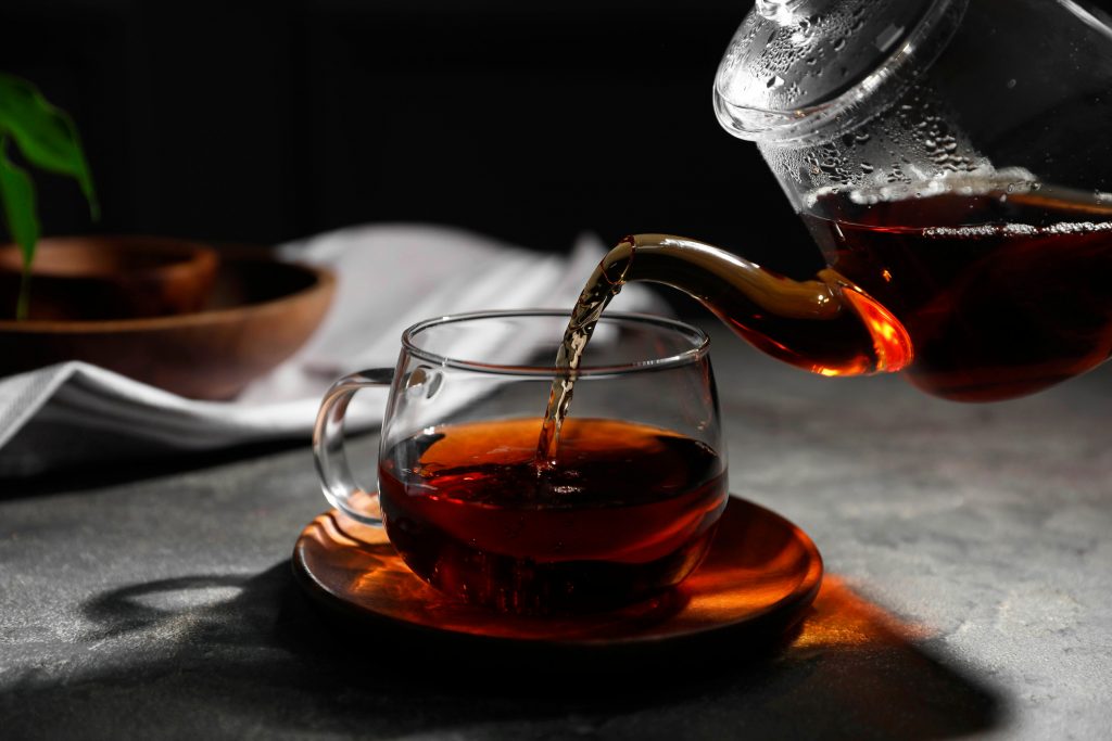 Pouring 100% oxidized black tea into cup on grey table, closeup