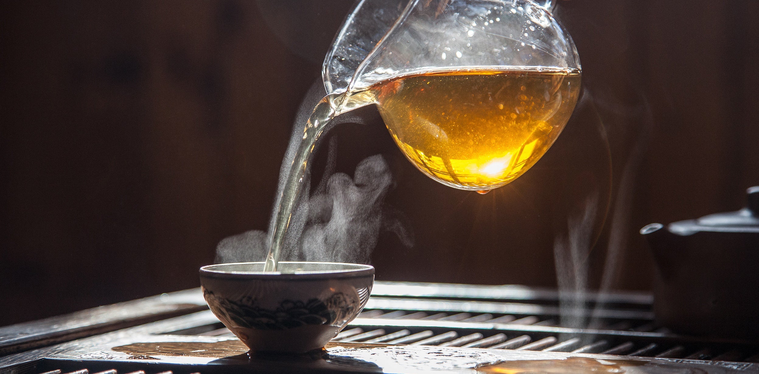 pouring hot tea from a decanter with the light shining through